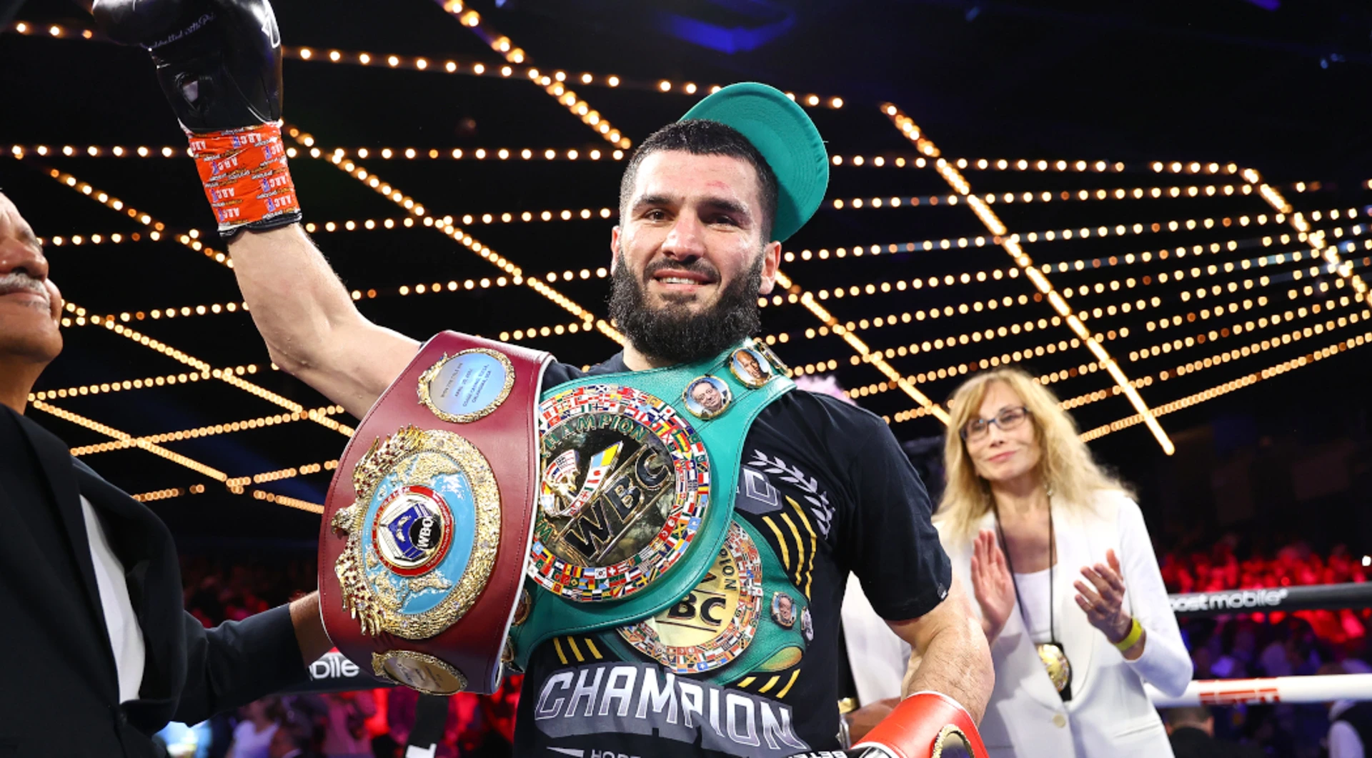 Artur Beterbiev com braço erguido e seus cinturões de campeão mundial de boxe nos ombros.